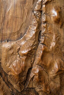  A map where hills, valleys, and rivers are carved into warm-toned wood — soft burnished highlights over mountains, riverbeds gouged gently into the grain — earthy, textured, permanent.