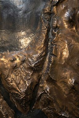  A heavy, shining map where mountains and ridges rise from darkened bronze or iron — rivers thin silver threads across hammered metal textures — weighty, monumental, luminous.