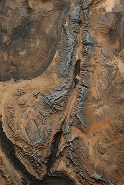  A deeply earthy map using mud-thickened paint and ash-blackened tones — mountains heavy with smeared gray ridges, plains smudged soft brown — terrain that feels pulled directly from the soil.