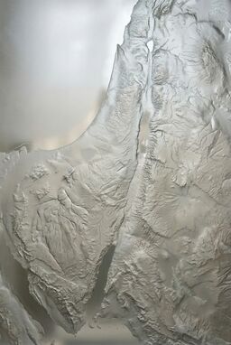  A modern take: a map where sandblasting erodes shallow terrain features into glass — rivers traced deeper, mountains subtly resisted — a wind-carved landform impression.