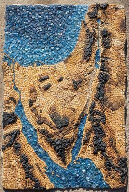  A terrain map built from tiny hand-cut stones — rough desert patches in warm ochre pebbles, riverbeds in glassy blues, mountains in rugged black — shimmering with uneven ancient energy.