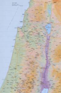 Full-color Carta atlas style with distinct hypsometric elevation tints, pale blue water, a pale blue-gray grid, ochre road lines, red dotted routes or boundaries, and dense black settlement labeling.