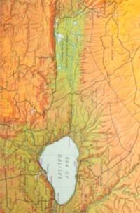 Full-color hypsometric terrain map with manual shaded relief, pale blue-green inland water, blue-green rivers, red settlement labels, black dot city symbols, and dark regional boundaries.
