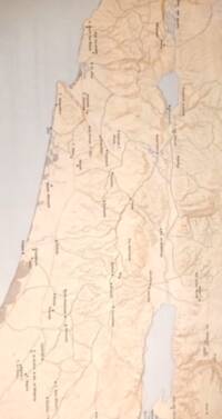 Visible style combines a warm bare-earth base, manual shaded-relief texture, pale gray-blue water bodies, and dense dark settlement labeling with small filled-dot point symbols.